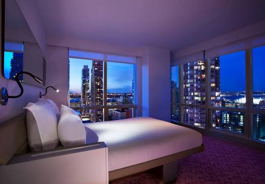 A compact cabin at YOTEL New York with a powered bed frame folding towards a sofa and a full-width window.